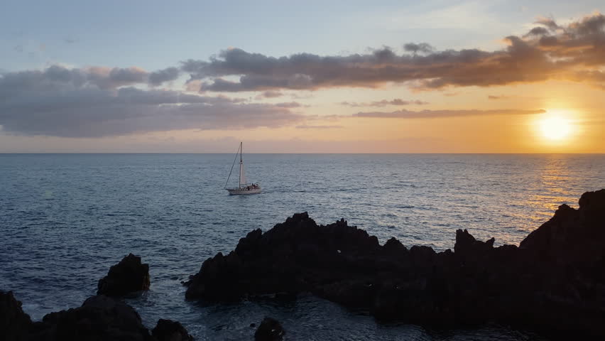 A landscape view of a boat sailing towards the rocks on the shore under the beautiful sunset light