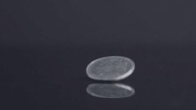A closeup footage of 1 rupee silver coin rolling on a reflective surface, isolated on a dark background - Powered by Shutterstock - Get 15% off with code: PIKWIZARD15