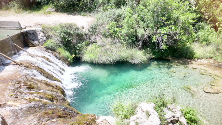A waterfall is flowing into a small pool of water. The water is clear and calm. The scene is peaceful and serene