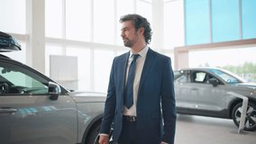 Zooming in on attractive Caucasian businessman or manager. Man wearing elegant blue suit while standing in auto showroom. Handsome male crossing hands and positively glancing at camera. - Powered by Shutterstock - Get 15% off with code: PIKWIZARD15