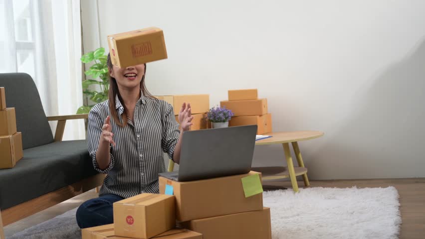  A woman is sitting at a desk with a laptop and a stack of boxes in front of her