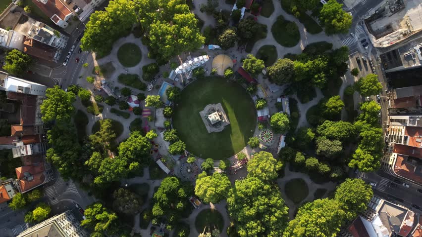 A timelapse top view of the Monument to the Heroes of the Peninsular War. Trees, roads with cars, and a ferris wheel around it.