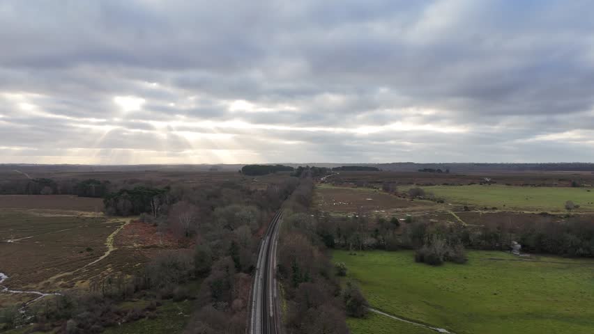 A drone footage of railway track between trees in a natural rural field on a cloudy day