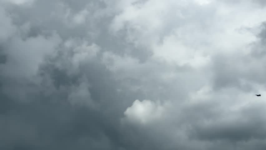 a fighter plane flying in the gray dense cloudy sky on the horizon