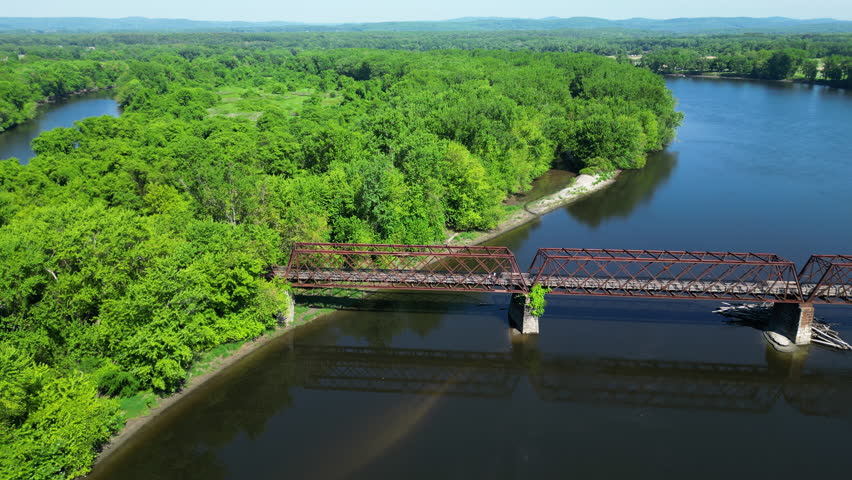 Aerial lateral shot of bridge over Connecticut River and green forest landscape. Norwottuck Rail Trail in Western Massachusetts