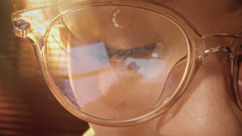 Close-up shot of woman eyes in glasses reflecting a working computer blue screen. Focused on work woman looking at laptop. Macro female eyes. Person watches hypnotizing index finger.