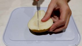 Hand slicing a pear on a cutting board