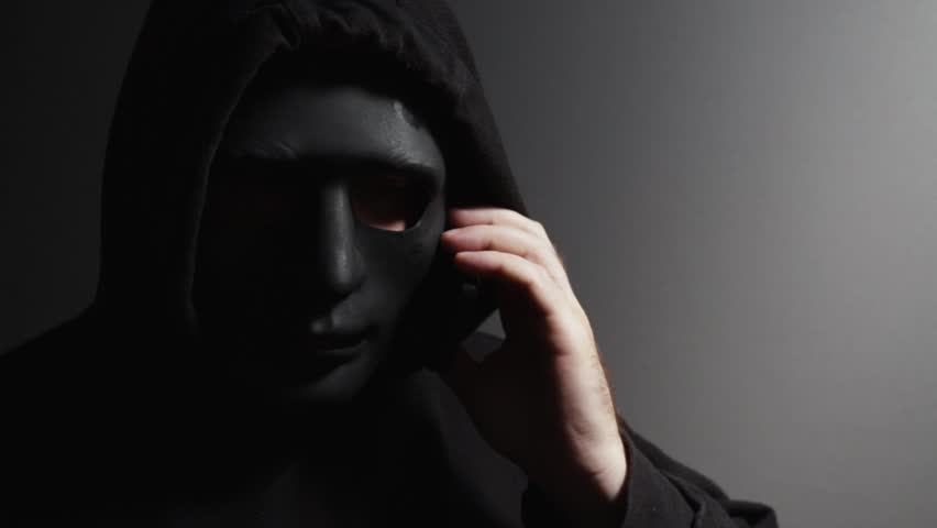Robber, a man in a mask talking on the phone, gangster planning theft, masked criminal plotting vandalism, felon discussing terrorism.
