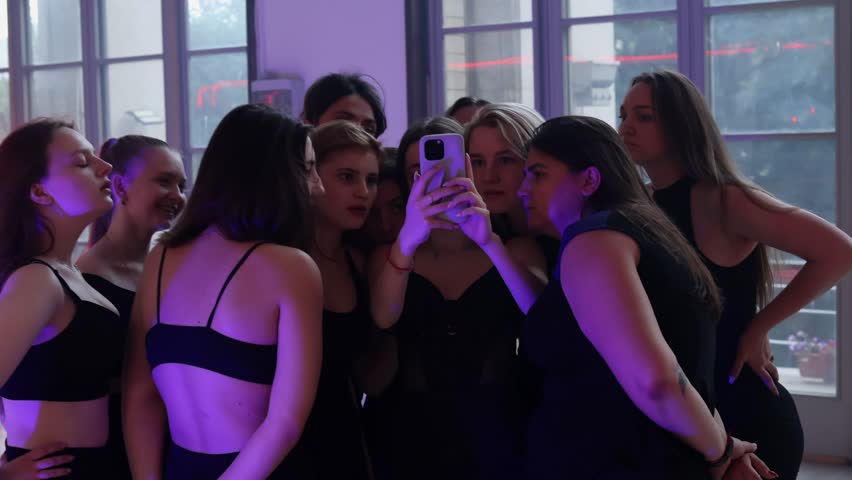 A group of female dancers gathered in a circle and are looking at a phone screen. Online dance lessons.