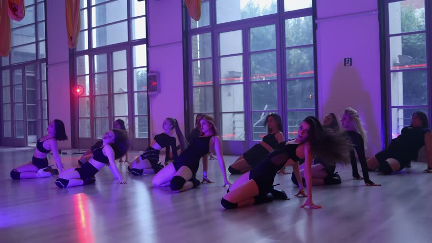 A group of 11 female heels dancers is dancing on the floor in a studio in the evening. Group heels dance lessons.