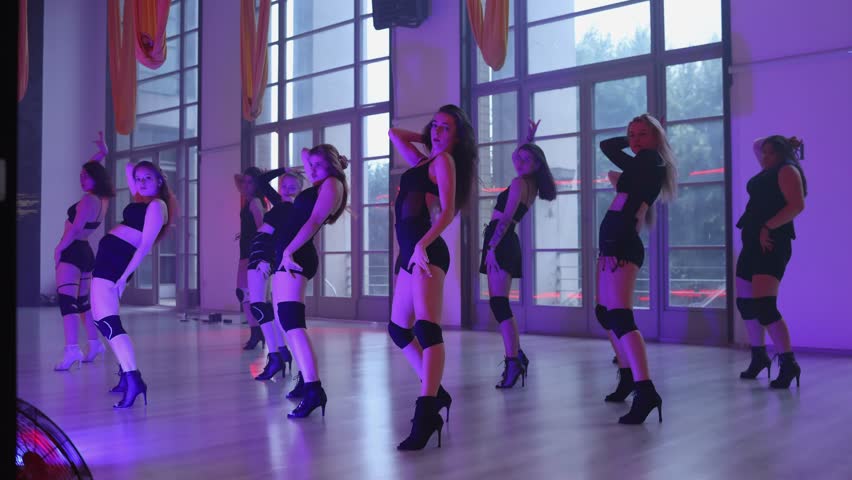 Group heels dance lessons. A group of girls dances in high heels under evening purple light.