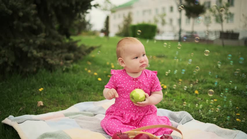 Young Girl in a Pink Dress Enjoying an Apple on a cloudy Day at the Park