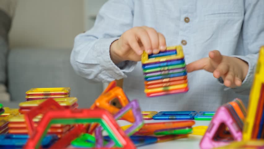 The child plays with a magnetic constructor, builds various figures while sitting at the table.