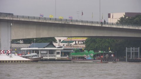 Boats under the Pinklao Bridge, Bangkok wait to dock while buses pass overhead.