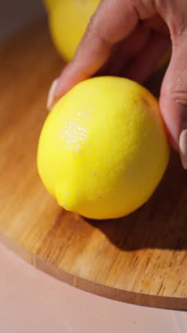 Female cutting into lemon over wooden cutting board, hard natural lighting