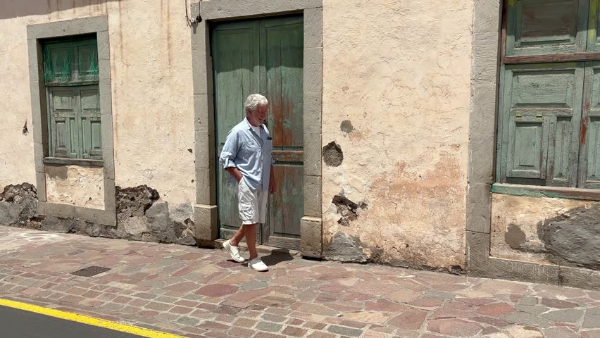 Elderly man walking in a city street answering mobile phone. Attractive senior man walking in Spanish city, close-up of smiling casual dressed man on urban background, portrait of attractive beard