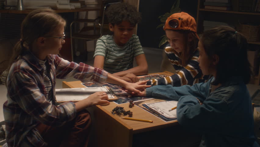 Medium shot of group of multiracial kids gathered to play board game at home in evening and putting hands together for lucky game