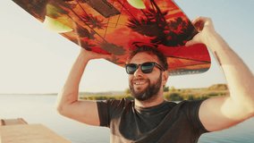 Portrait of a smiling and happy surfer-wakeboarder with a colored board he is holding above his head. - Powered by Shutterstock - Get 15% off with code: PIKWIZARD15