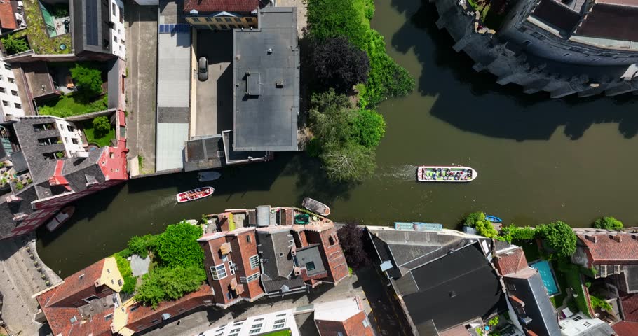 Lieve Canal by Gravensteen Castle, East Flanders, Ghent, Flemish Region, Belgium, June 2022. Drone in Birds Eye View following tourist boats slowly taking in the sights along guided architecture tour.