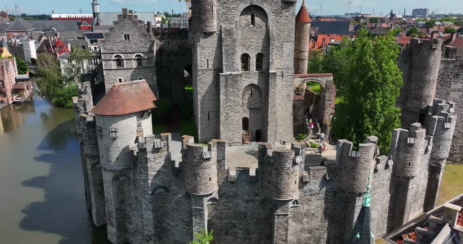 Gravensteen Castle, East Flanders, Ghent, Flemish Region, Belgium, June 2022. Drone pulls back revealing the iconic moat brick walls with flags waving proudly in wind over the city.