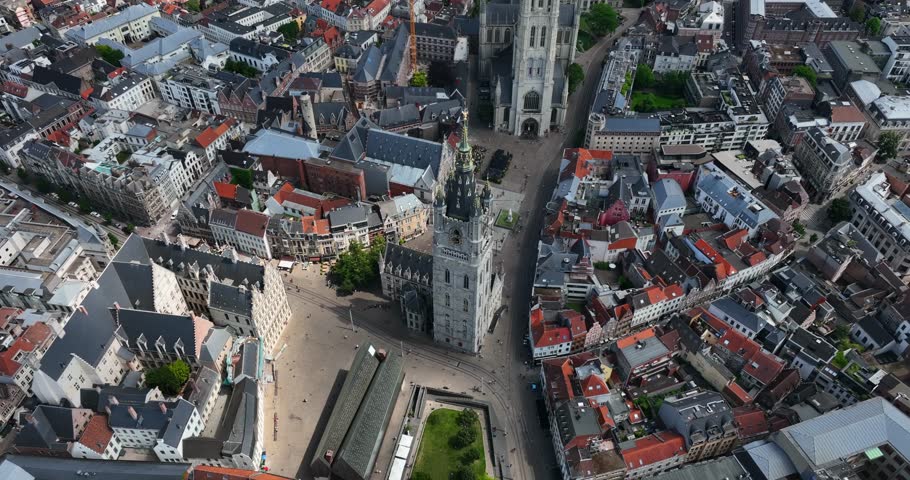 Belfry of Ghent, East Flanders, Ghent, Flemish Region, Belgium, June 2022. Drone orbits as moody cloud shadow darkens town and sidewalk roads around the row of three.