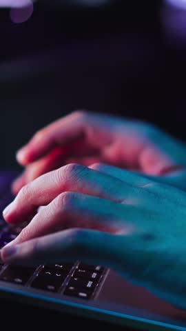 Vertical close up of unrecognizable young man hands typing on laptop keyboard in dark room. Caucasian male professional freelancer using computer working as hacker programming new code security system