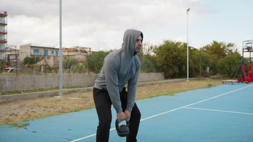 Athlete Man Trains With Kettlebell Weight In Blue Field Outside
