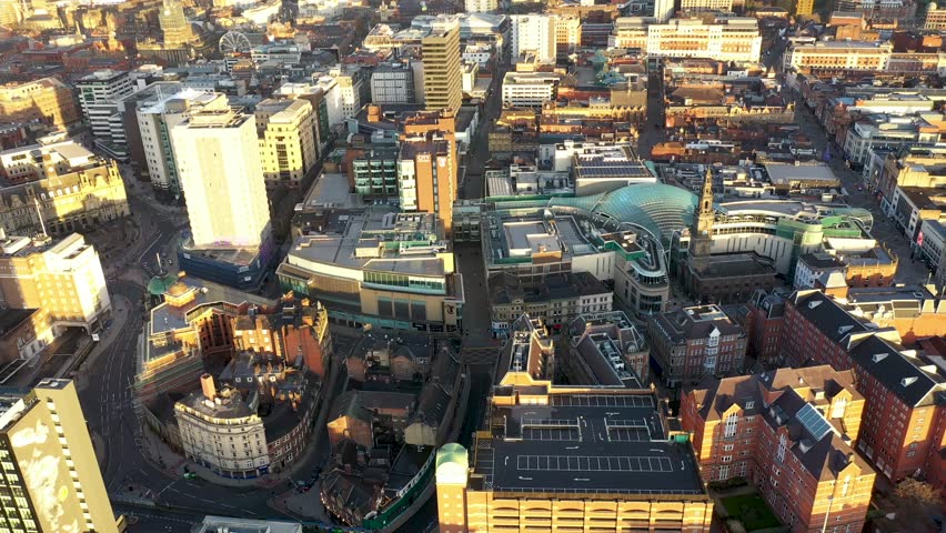 Aerial drone footage of the town centre of Leeds in West Yorkshire UK, showing the whole of the Leeds City Centre and the glass building of the Trinity centre, taken at sunrise with the sun reflecting