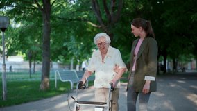 Young woman walking with her elderly grandmother in city park. Senior woman using mobility walker, enjoying good company and warm weather. - Powered by Shutterstock - Get 15% off with code: PIKWIZARD15