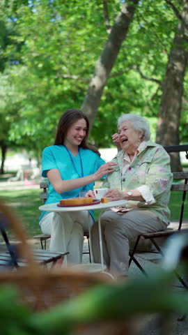 Nurse sitting on coffee with elderly woman in city park. Senior woman enjoying good company and warm weather.