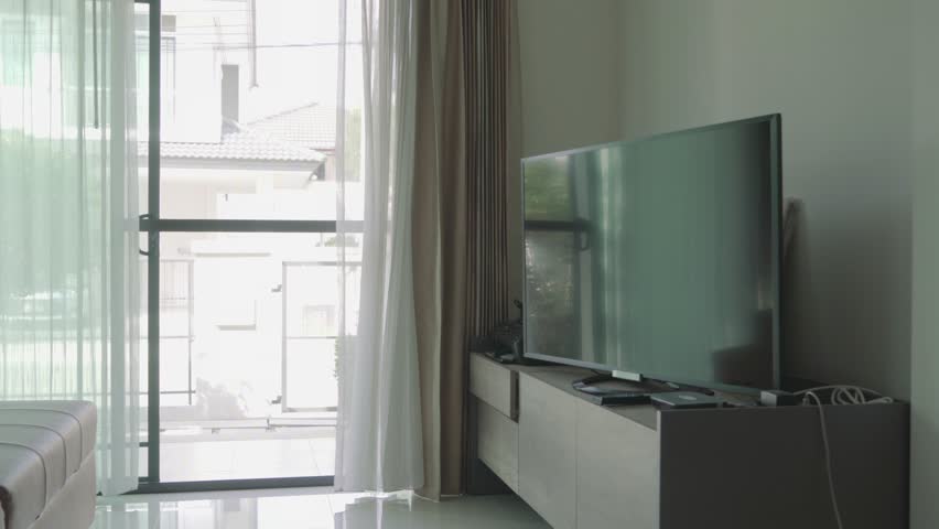 A living room with a large flat screen television on a wall. The room is bright and airy, with a large window letting in plenty of natural light
