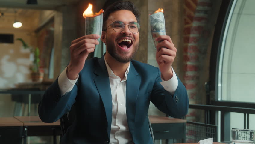 Happy male Arabian Indian business man crazy mad laughing guy joyful excited businessman office investor rejoicing fooling burn money dollars waste finance cash salary enjoy burning banknotes have fun