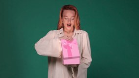 A delighted woman in a cream outfit opens a pink gift box with a ribbon, showcasing a moment of surprise and joy. The vibrant blue background highlights her cheerful expression. - Powered by Shutterstock - Get 15% off with code: PIKWIZARD15