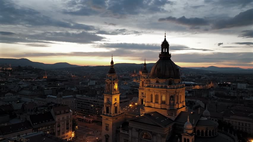 Aerial video about illuminated  St Stephens basilica at dusk. Hungarian Parlament's building is on the background
