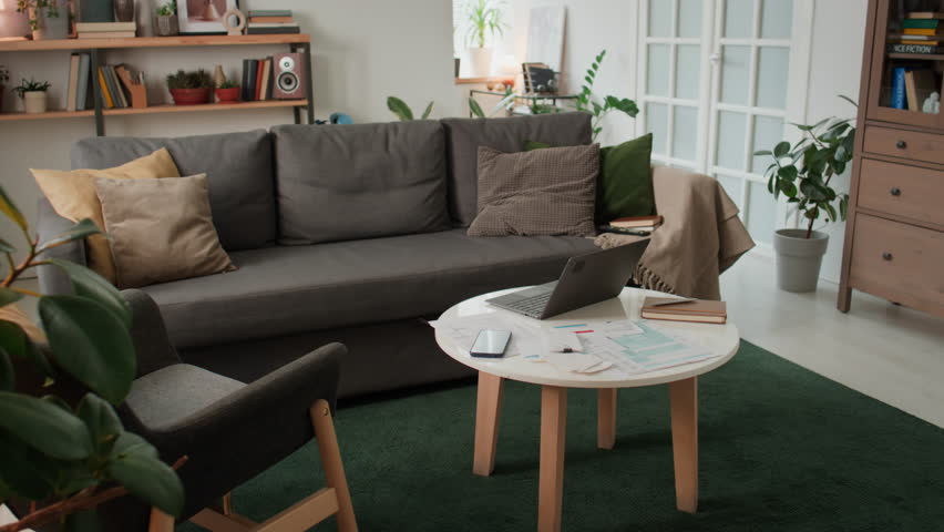 Full pan no people shot of living room in young family home, with couch, table with lots of financial documents, bills, invoices, laptop, with green carpet, on Sunday morning