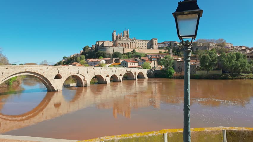 Cityscape of Beziers old town in spring season in France. The old bridge over the Orb river with the Cathedral of Saint Nazaire in Beziers, Southern France. Slow motion revealing footage.