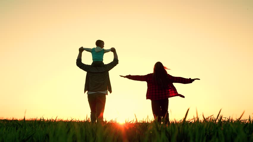 Cheerful mother father child kid running across field towards orange sunset. Child kid sits on shoulders of dad mother mom runs with arms outstretched. Happy family spends fun time in nature running,