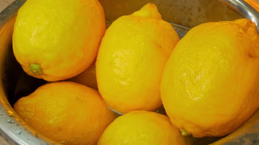 Several lemons are washed with hot water in a metal bowl