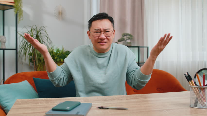 I don't know what to say. Confused Asian middle-aged man feeling embarrassed about ambiguous question, having doubts, no idea, being clueless and uncertain. Mature Chinese guy at home room on couch