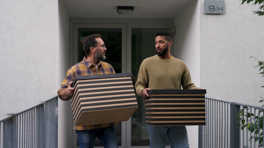 Man helping his friend move into new apartment in building. Man is moving into new flat, carrying box from the moving truck.