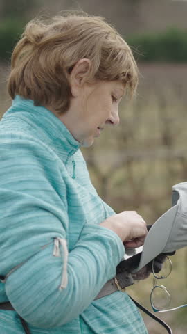 Caucasian woman standing in the vineyard typing a message with her smartphone with her cap and glasses in her hand