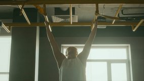 Medium full backlit shot of young muscular biracial female boxer performing set of pull-ups on monkey bars at sports gym with body weight, against bright daylight in window, to improve strength - Powered by Shutterstock - Get 15% off with code: PIKWIZARD15