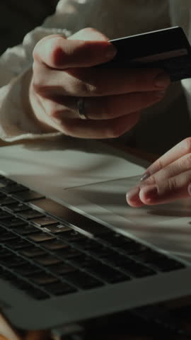 Vertical video. Online payments, e-commerce ordering concept. Female hands enter payment card details using laptop.