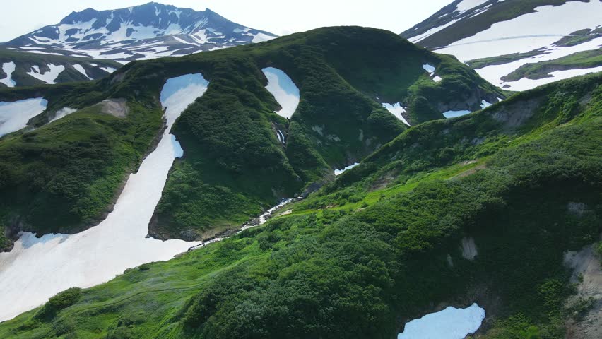 Small valley of geysers in Kamchatka, Russia. Green mountains and volcanoes with snow. Aerial drone view. Beautiful summer landscape. 

