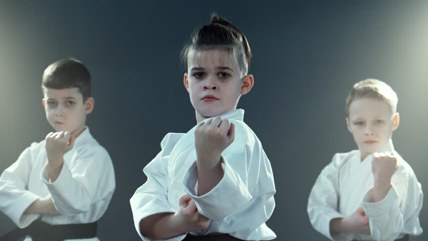 Boys training karate at smoky background. Group of young karate practitioners in white kimono, perform synchronized martial arts katas. Practicing karate moves at class indoors