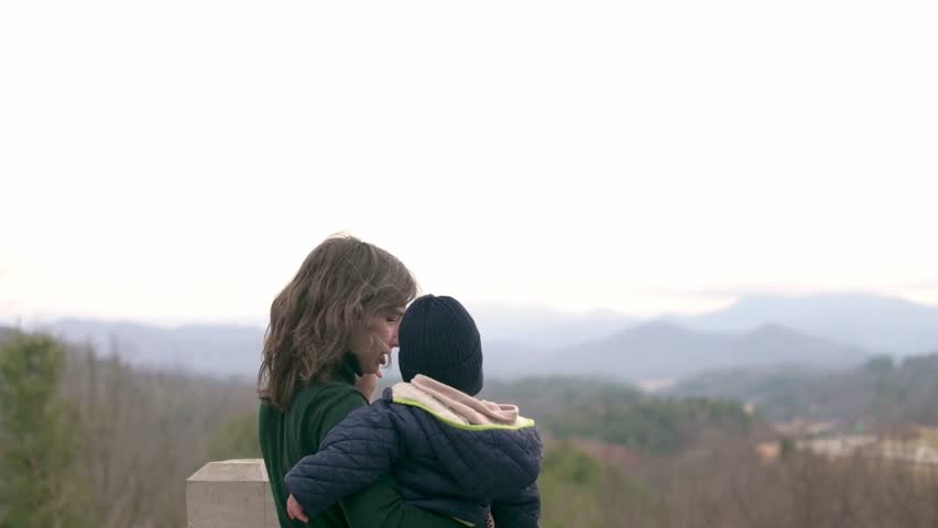  Mother holding her baby while enjoying a scenic view of the Blue Ridge Mountains on a cloudy day, capturing a tender and serene moment.