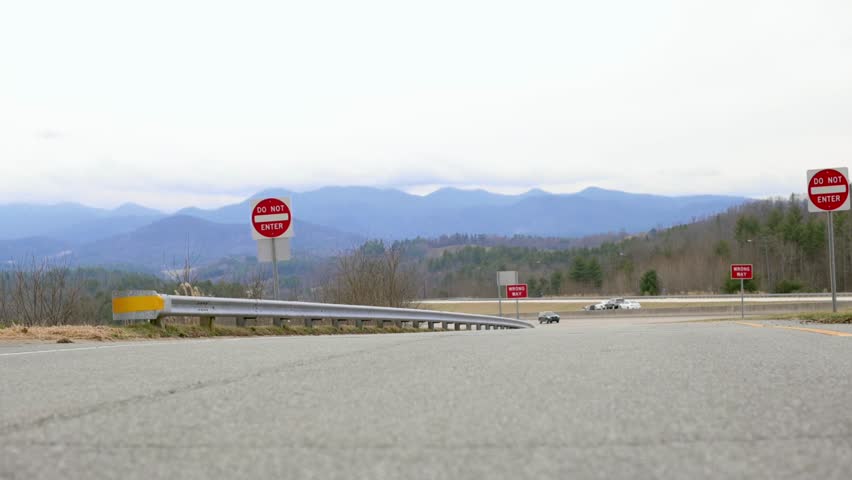  A rural road featuring multiple stop signs, with a scenic view of the Blue Ridge Mountains in the background on a cloudy day.