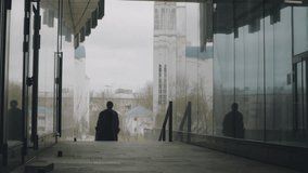 Full shot of young Asian man in long trench coat walking between two glass walls on city street - Powered by Shutterstock - Get 15% off with code: PIKWIZARD15