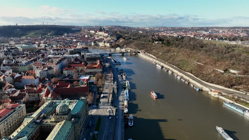 Prague, Czechia, December 2022. Drone tracks over the Vltava river looking west towards the Svatopluk Čech Bridge with Petrin Hill and Prague Castle in the distance.