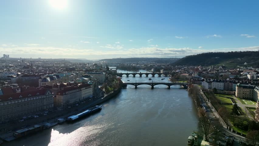 Prague, Czechia, December 2022. Drone tracks across the Vltava river looking towards the Mánes Bridge with the Charles Bridge in the distance on a winter sunny day.